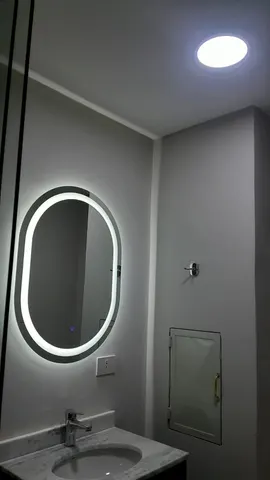 Baño con espejo ovalado retroiluminado con LED y plafón en el techo