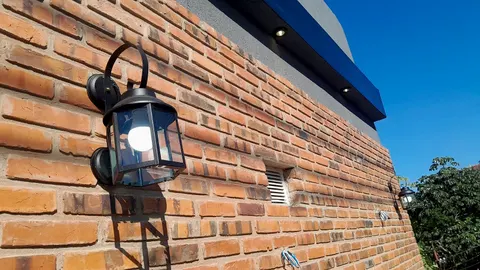 Farol de pared negro instalado sobre una fachada de ladrillo visto