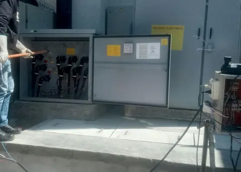 Técnico con guantes y pértiga aislante frente a una celda de transformación abierta